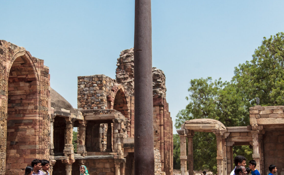 Iron Pillar of Delhi, Qutub Minar complex, ancient metallurgy, Indian history, historical monument, Delhi, India, ancient architecture, tourists, clear sky, heritage site, archaeological site, iron pillar, Ashokan pillar.