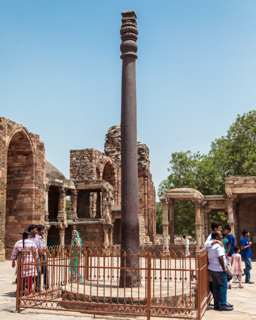 Iron Pillar of Delhi, Qutub Minar complex, ancient metallurgy, Indian history, historical monument, Delhi, India, ancient architecture, tourists, clear sky, heritage site, archaeological site, iron pillar, Ashokan pillar.